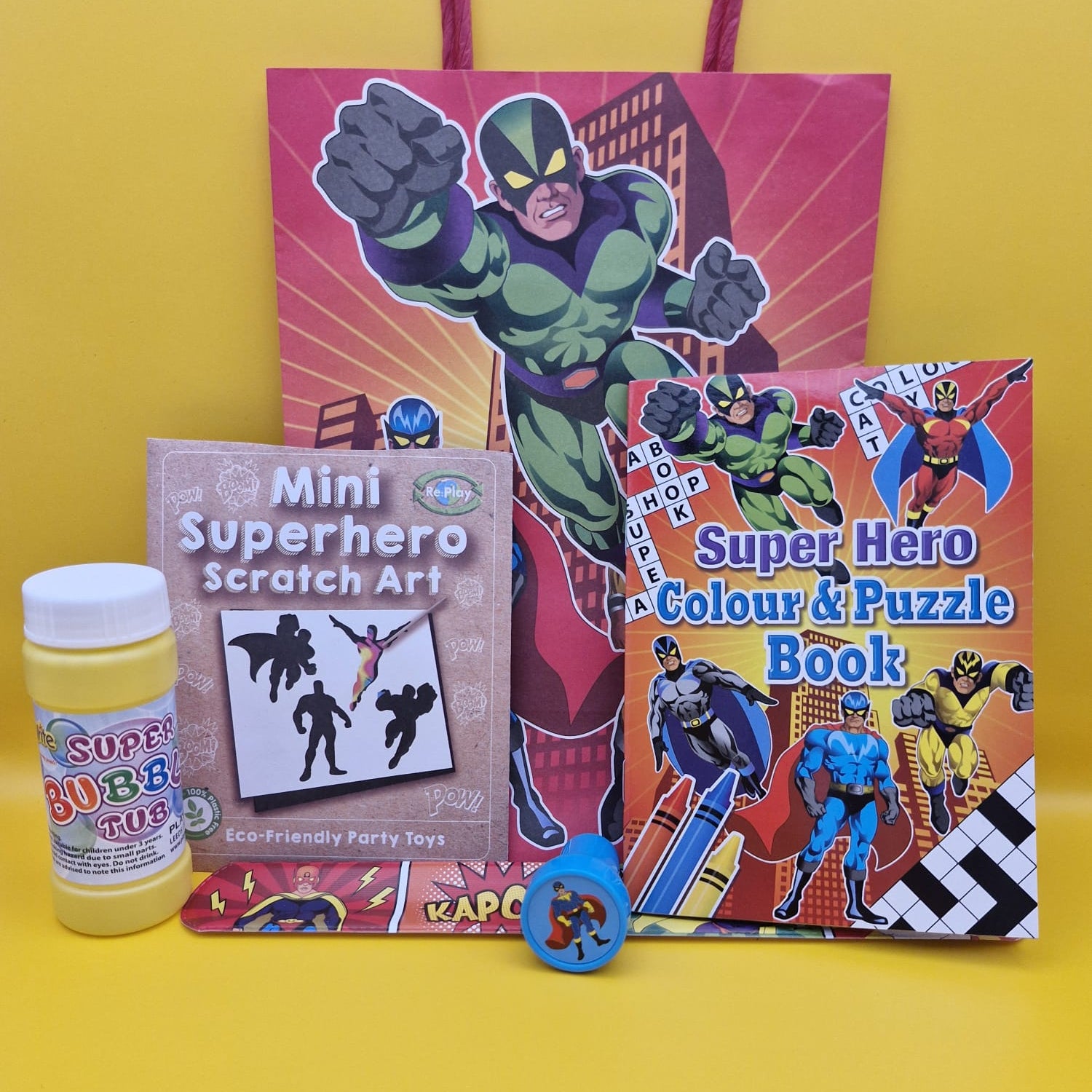 Superhero-themed children's colouring book, scratch art kit, and toy on a yellow background