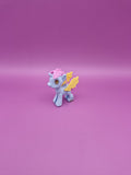 Small toy unicorn with pink hair and yellow wings on a pink background