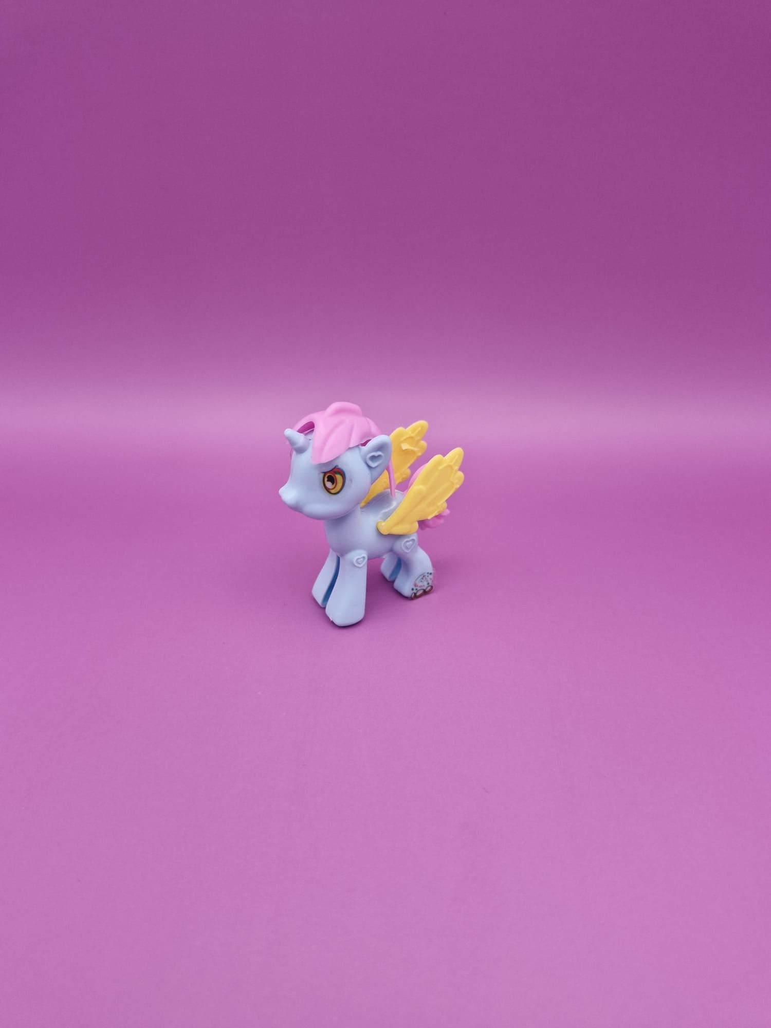 Small toy unicorn with pink hair and yellow wings on a pink background
