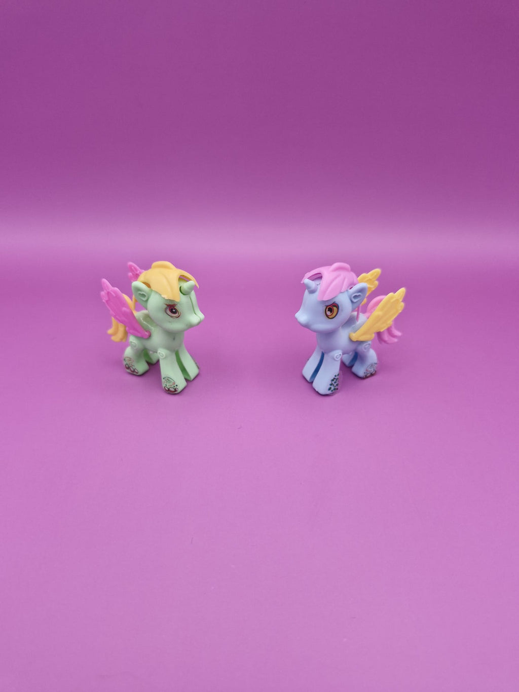 Two small unicorn figurines on a pink background