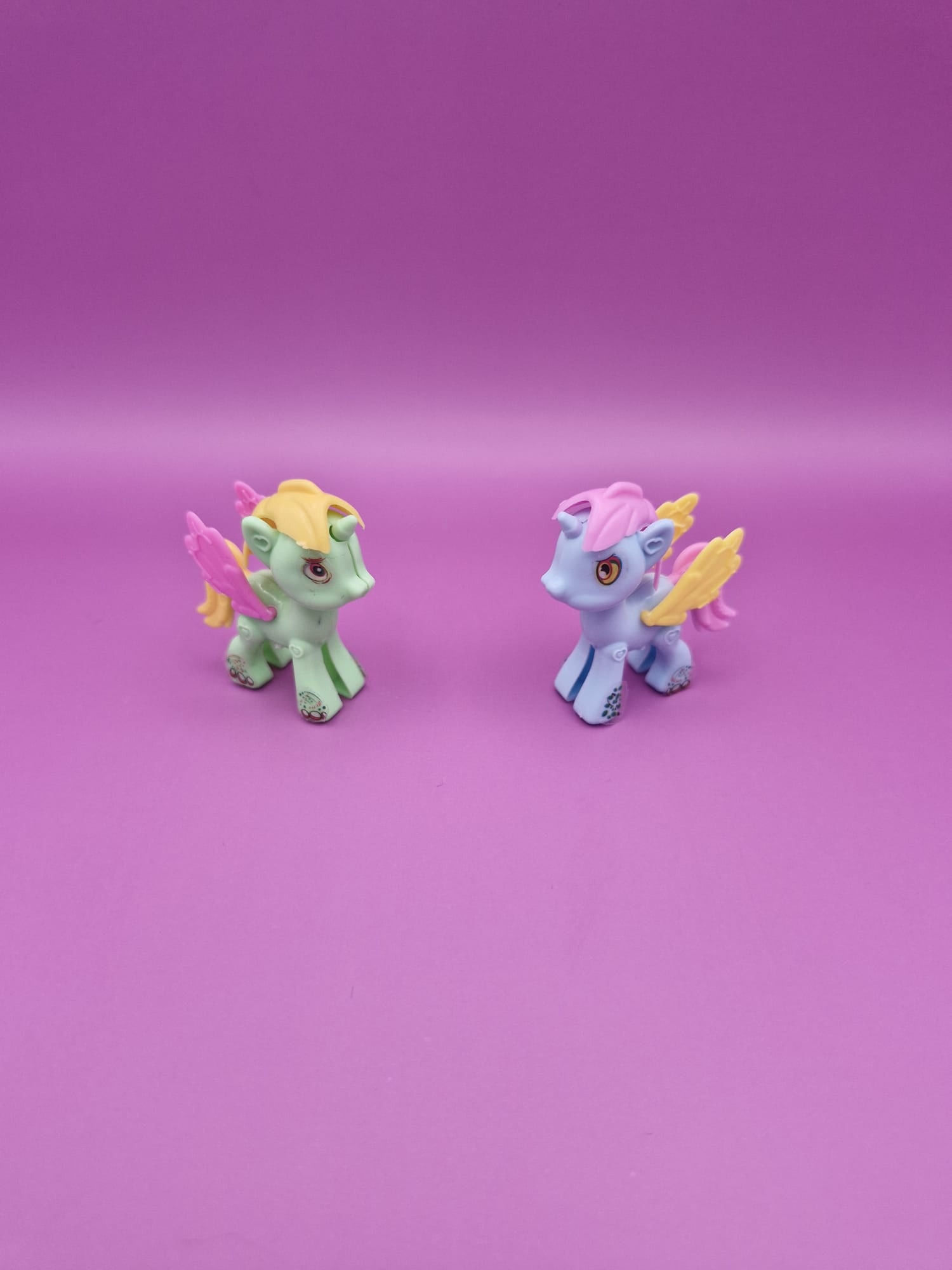 Two small unicorn figurines on a pink background