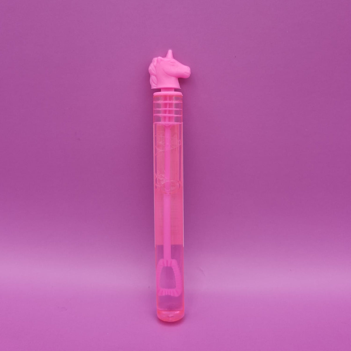 A pink unicorn-shaped bubble wand with a clear plastic tube and pink bubble solution, set against a solid pink background.