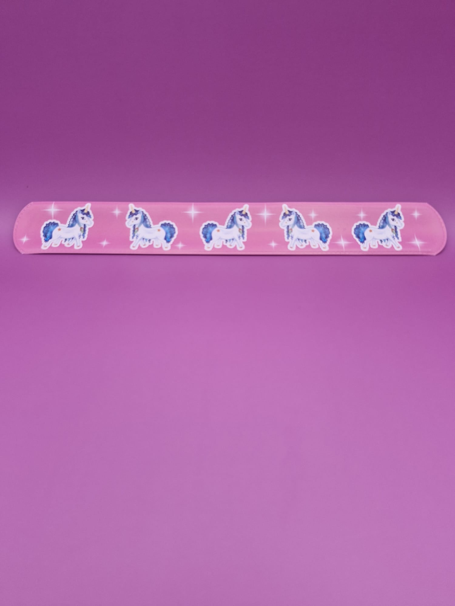 Pink snap bracelet with unicorn designs on a purple background